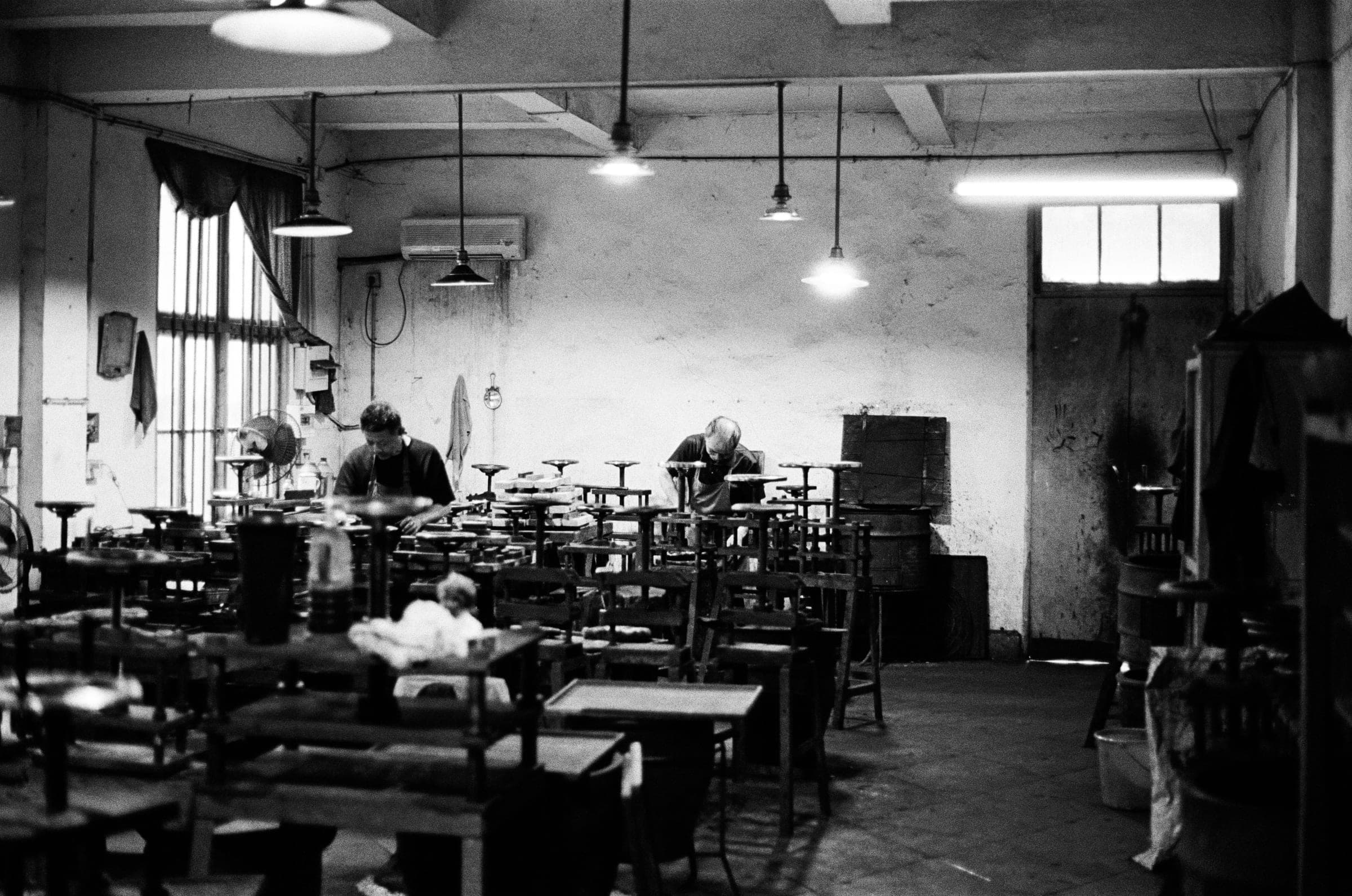 Two people among rows of tables and stools in an old canteen, black and white