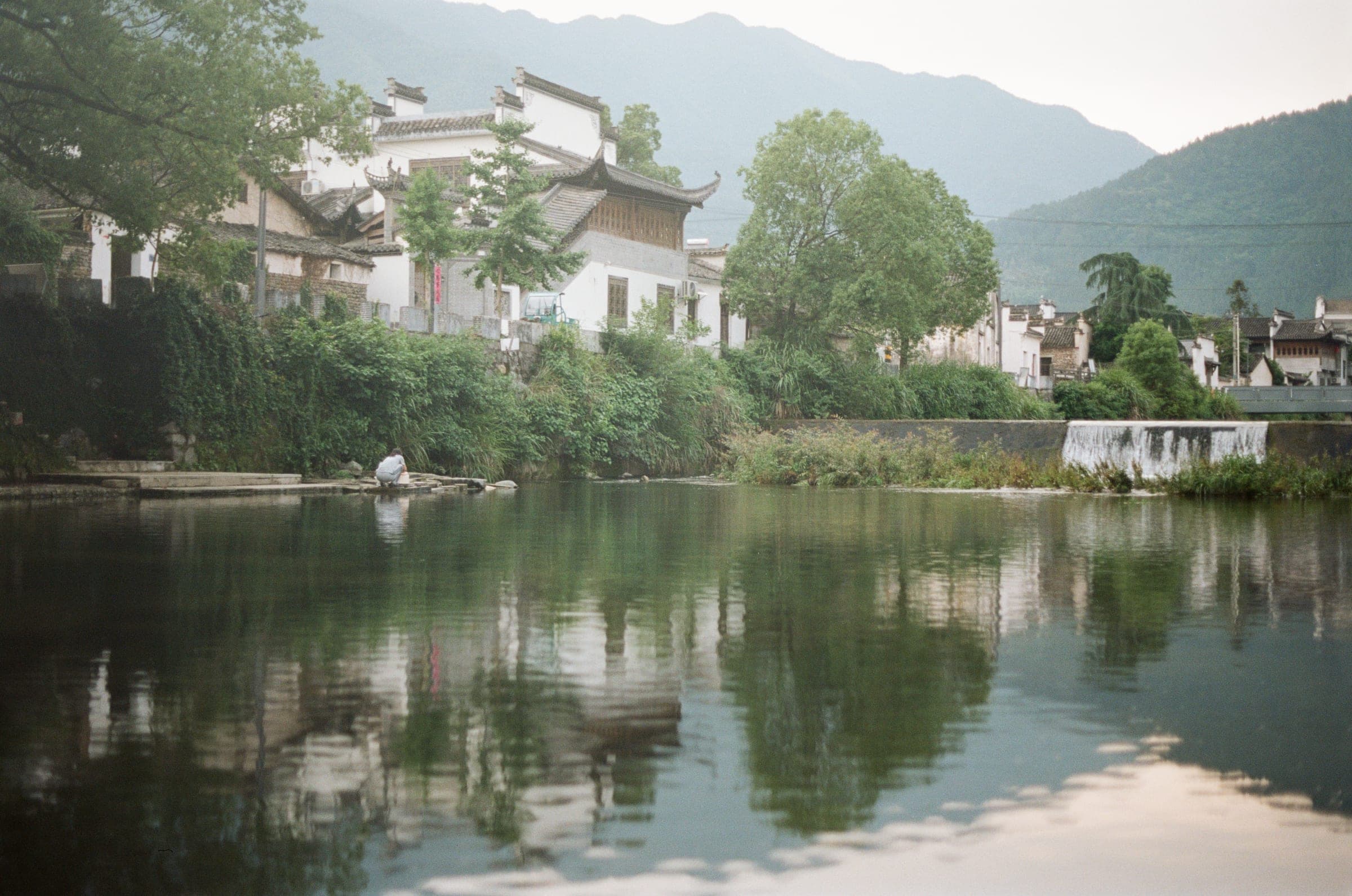 Village houses and trees reflected in a still river, Huangshan
