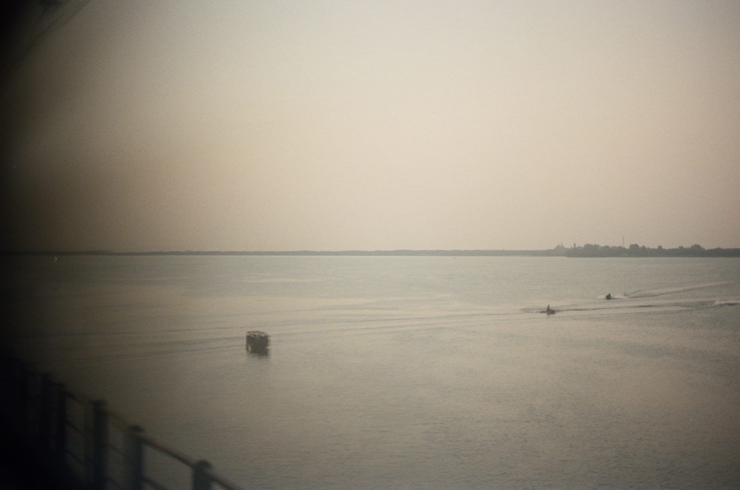 Small boats on a wide, hazy river seen from a ship's deck